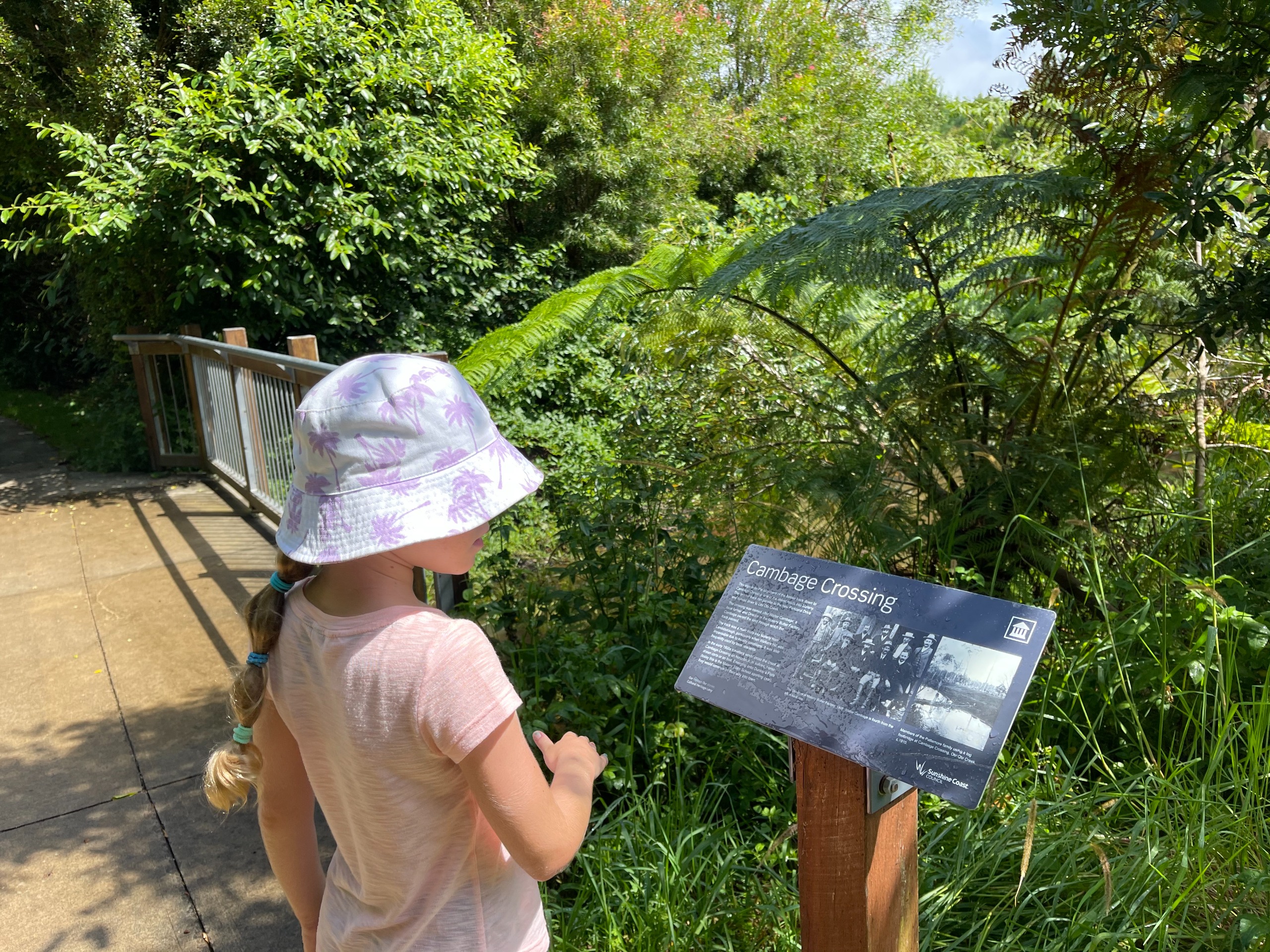 Image of small girl looking at intepretative signage infront of plants outdoors.