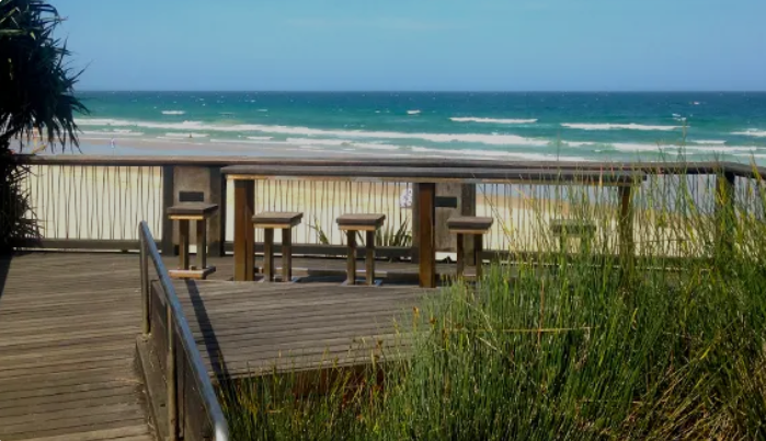 Timber viewing deck with chairs and stools overlooking the ocean.